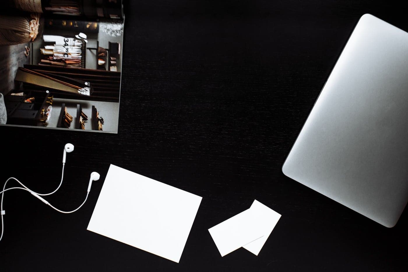 A laptop, printed cards and headphones on a dark desk