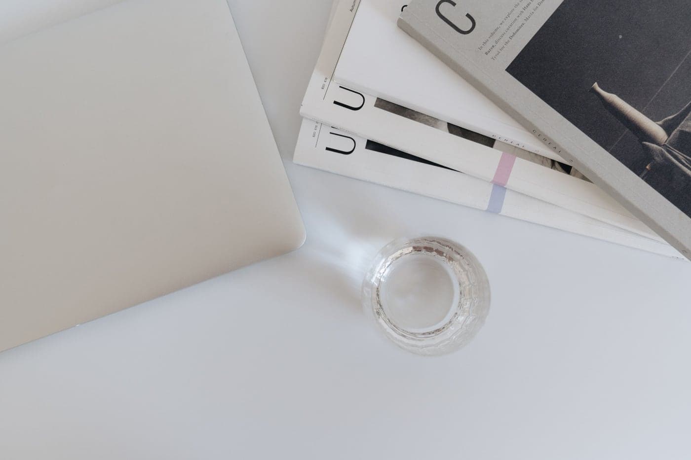 A minimal pale desk with a magazine and a glass of water